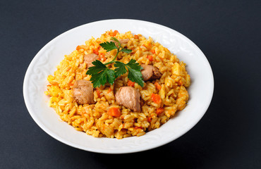 white plate of cooked rice with meat on dark background