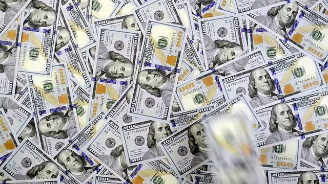 Hundred dollar banknotes falling on a table surface covered with cash. The money bills fall one at a time. 