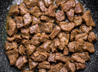 pieces of meat are fried in a frying pan.