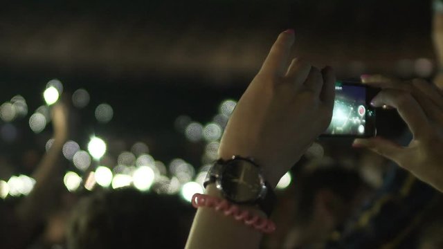 Female hands holding smartphone, woman in crowd filming video of amazing event