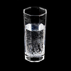 A glass of pure sparkling mineral water on black background close-up.