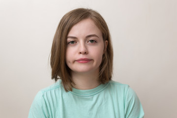 A full face of a blond girl wearing blue t-shirt with annoyed, funny, bored, tired or face-palm expression on her face with white background and warm, soft colors