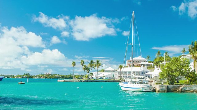 St. George's Harbor in Bermuda with a Ferry Crossing in the Background, featuring Turquoise Colored Water, Green Palm Trees, Bermudan Architecture, a Yacht, and White Clouds in a Blue Sky