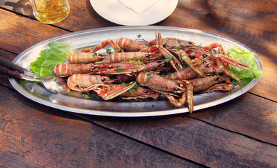 Large prawns with shells, fried in olive oil with garlic and parsley on a metal dish. Wooden table in a cafe.