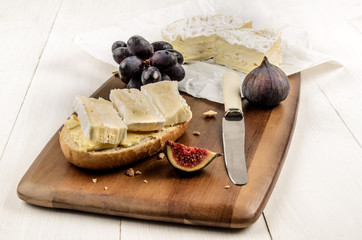 half bun with camembert on a wooden board, also with a fig and r