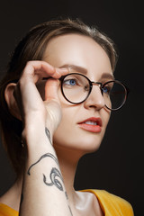 Fototapeta premium Portrait of suspicious girl in spectacles in dress with tattoo o