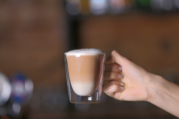 Female hand holding cup of hot coffee in cafe