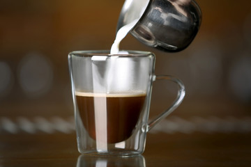 Pouring milk in cup of coffee, closeup