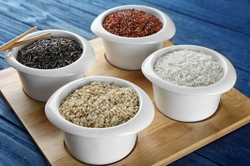 Different types of rice in bowls on wooden tray closeup
