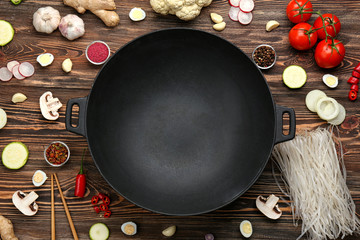 Empty wok pan with fresh ingredients on wooden background, top view