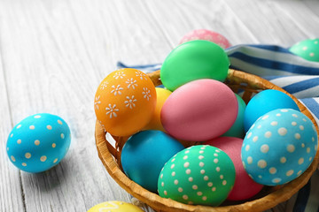 Fototapeta na wymiar Basket with colorful Easter eggs on wooden table, closeup
