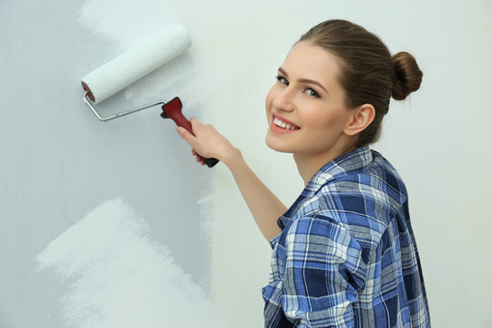 Beautiful young woman painting wall in room