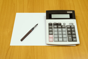 Brwon pen and a calculator on a plain white paper with a wood desk as background