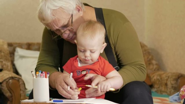 Attractive baby drawing with markers on paper with his grandfather. The child is allergic and reddened eyes. Kid 1 year.