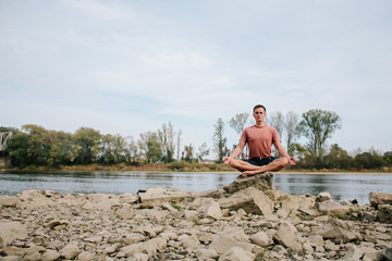 man practices yoga on the river bank