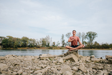 man practices yoga on the river bank