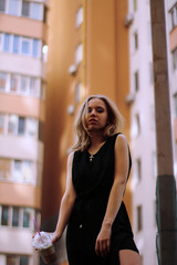 girl in a black dress with a cocktail in a residential area on the background of a house. 