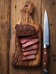 Single roasted medium rare sliced flank beef piece with herbs over wooden bord