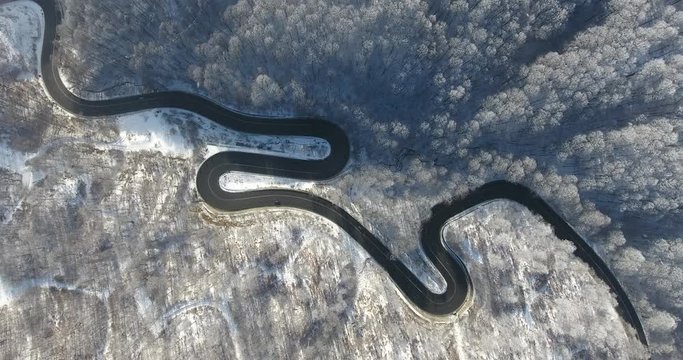 Winter winding road trough the forest in Transylvania. Aerial footage from a drone. Snow covered trees and mountains visible