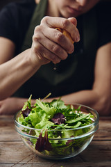 Woman chef in apron dressing salad with lemon on wooden board. Vegan meal.  