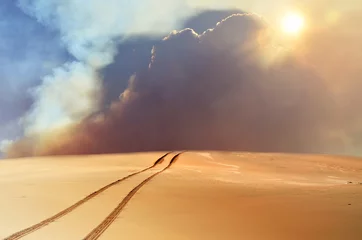  Voertuigsporen door woestijn en duinen leidend naar een met zand, rook en wolken gevulde lucht. © KHBlack