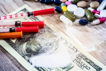 Injection syringe with cocaine drug powder and pills, dollar money bills.