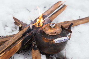 Copper kettle over an open fire in winter. Boiling kettle on firewood. Open fire cooking. Snow around. Lifestyle, camping. Blurred background.