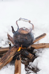 Copper kettle over an open fire in winter. Boiling kettle on firewood. Open fire cooking. Snow around. Lifestyle, camping. Blurred background.