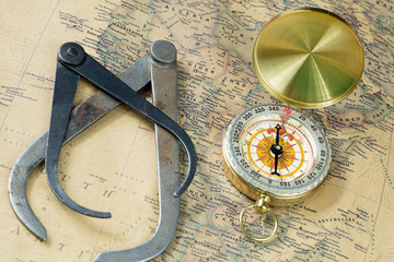 The old measuring tool gold compass with cover on vintage map, macro background, compasses