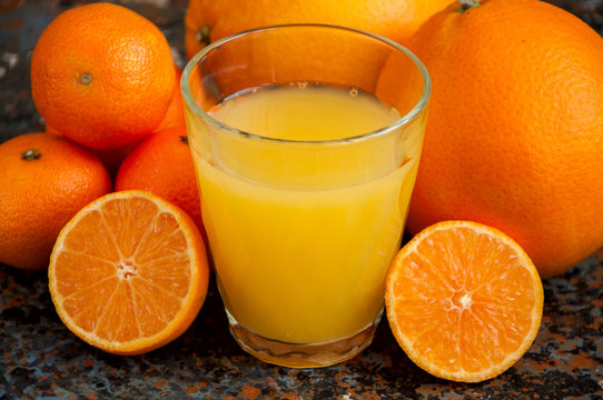 Orange and tangerine juice in a glass on a rusty background