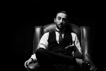 Fototapeta na wymiar side view of an elegant young businessman smoking a cigarette on black studio background