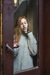 Sensual redhead  model with freckles behind the old  glass door