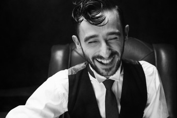 close portrait of handsome male model in black suit fixing his red tie while looking at the camera in smile