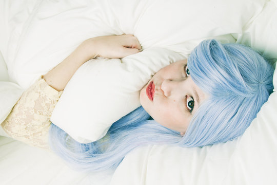 Chica joven con el pelo azul metida en su cama 