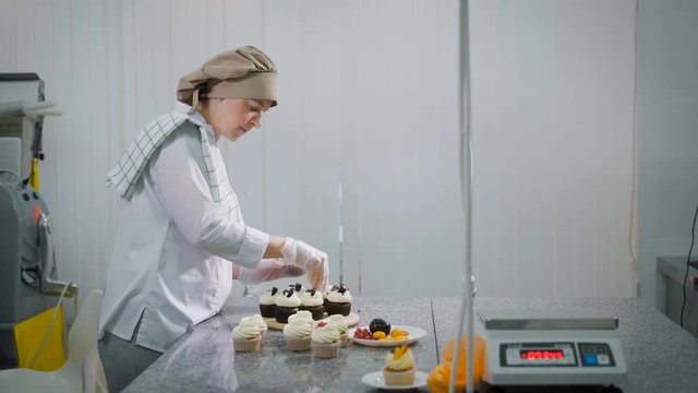 The woman cooks cakes for a holiday. At the girl the order as the candy store is small business. Cakes are ready on a table. On a table chocolate and fruit cupcakes.
