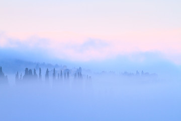 Fototapeta premium Tuscan landscape with country houses and cypresses in the fog