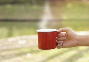 hand holding red coffee cup in blur green gardent background