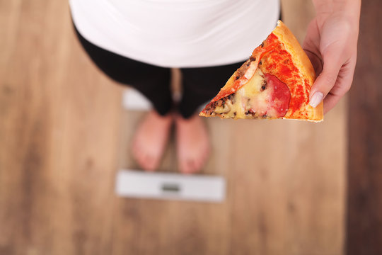 Diet. Woman Measuring Body Weight On Weighing Scale Holding Pizza. Sweets Are Unhealthy Junk Food. Dieting, Healthy Eating, Lifestyle. Weight Loss. Obesity. Top View