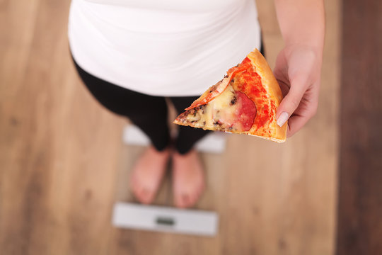 Diet. Woman Measuring Body Weight On Weighing Scale Holding Pizza. Sweets Are Unhealthy Junk Food. Dieting, Healthy Eating, Lifestyle. Weight Loss. Obesity. Top View