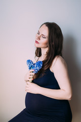 Pregnant woman with closed eyes in dark blue dress sitting with bouquet of flowers