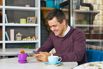 Young man holding a mobile phone and smiling. Read the posts and drinking coffee.