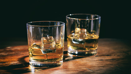 Glasses whiskey and ice cubes on wooden counter