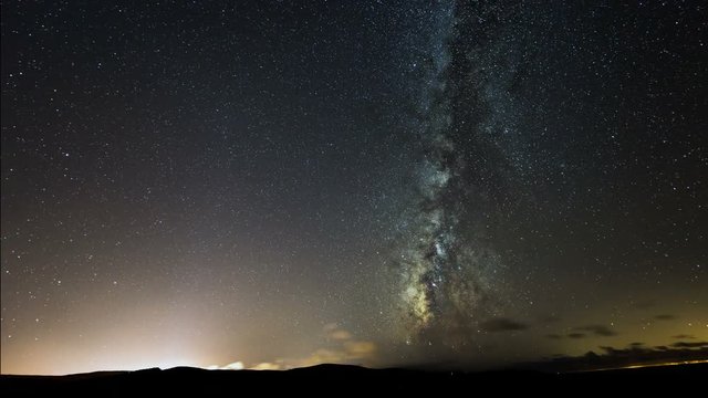 A 4k UHD time lapse shot of the milky way at night with a city light and some clouds. 11101
