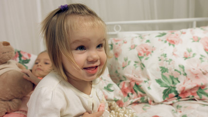 Naklejka premium Adorable little girl sitting on a bed with her sister