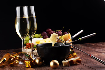 Gourmet Swiss fondue dinner on a winter evening with assorted cheeses on a board alongside a heated pot of cheese fondue with two forks dipping bread and white wine behind in a tavern or restaurant