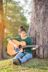 Young asian girl in forest with guitar, selective focus