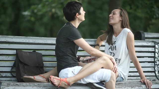 Beautiful happy lesbians relaxing on bench in park