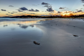 Fototapeta premium Scenic and pristine white sandy beach with turquoise crystal waters and orange lichen covered granite boulders at sunset. The Gardens in the Bay of Fires consevation Area, east coast of Tasmania.