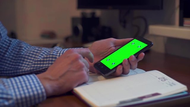 Man holds in his hands a smart phone with green screen.