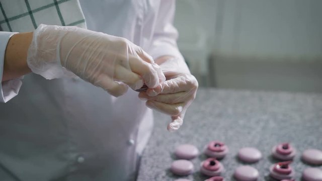 Candy store. Decoration of the French macaroons. The worker of a candy store in gloves adds cream and berries to a ready dessert. Thus decorating a dessert. A dessert have turned out pink-lilac color.
